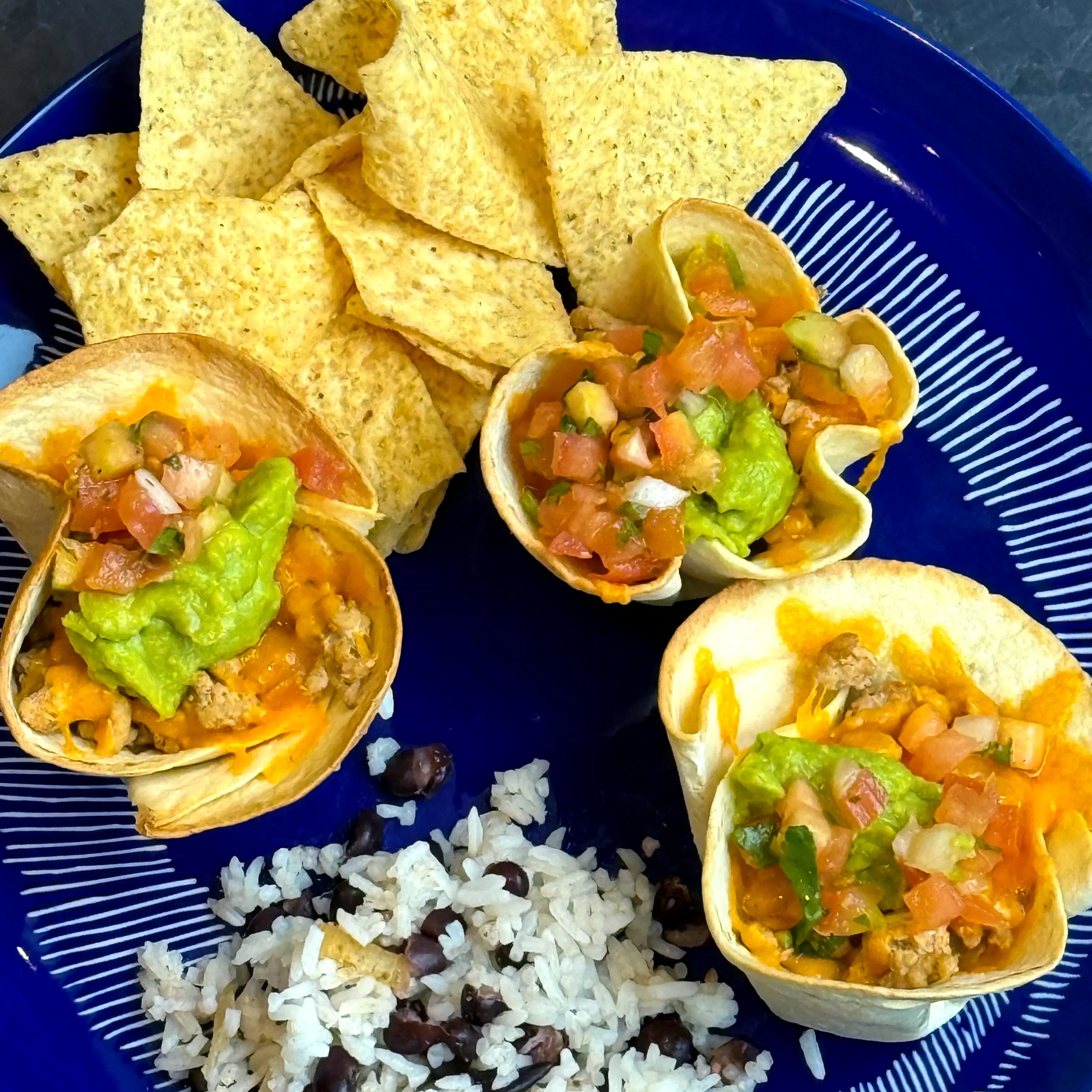 Taco bowl with tortilla chips, rice and toppings on a blue plate