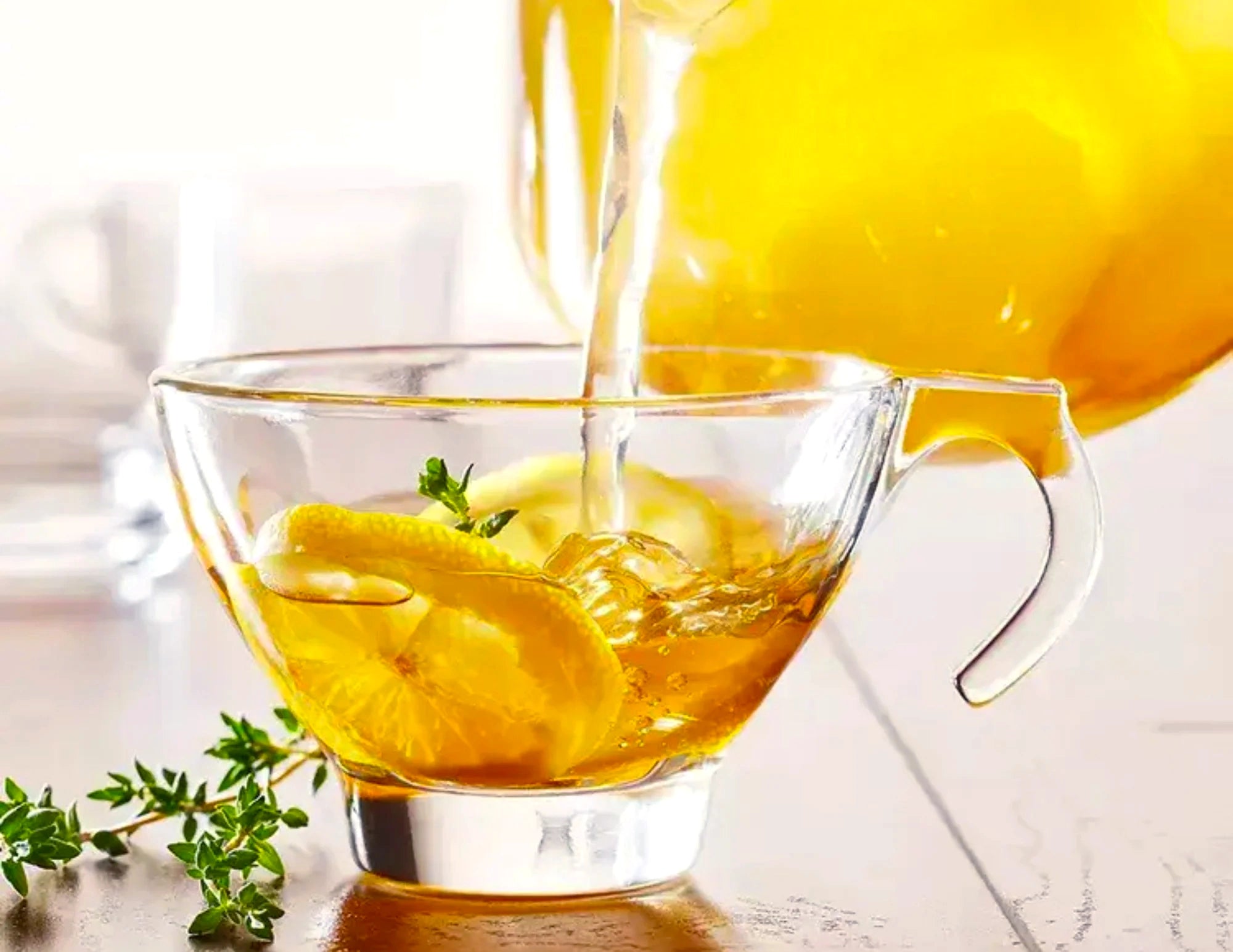 Honey citrus tea being poured into a glass teapot with lemon