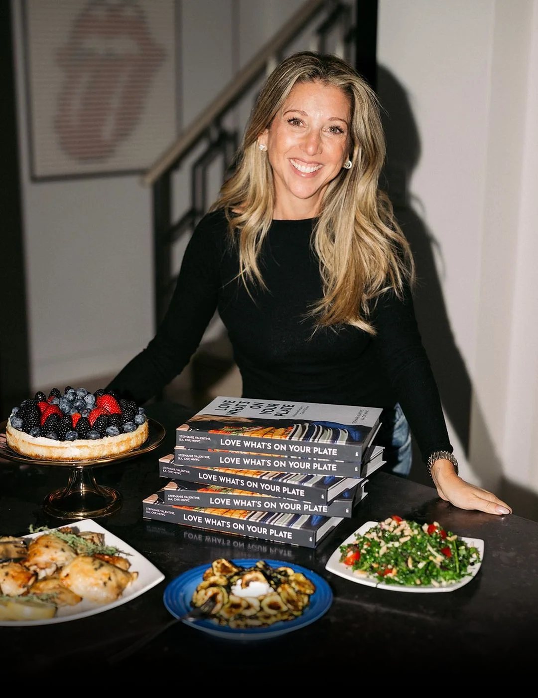 Stephanie Valentine with a stack of her cookbook Love What's On Your Plate and dishes from it